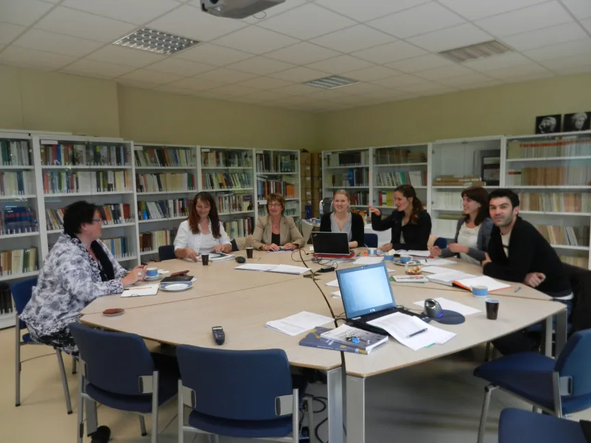 Sieben Menchen sitzen rund um einen großen Tisch in einem Büro