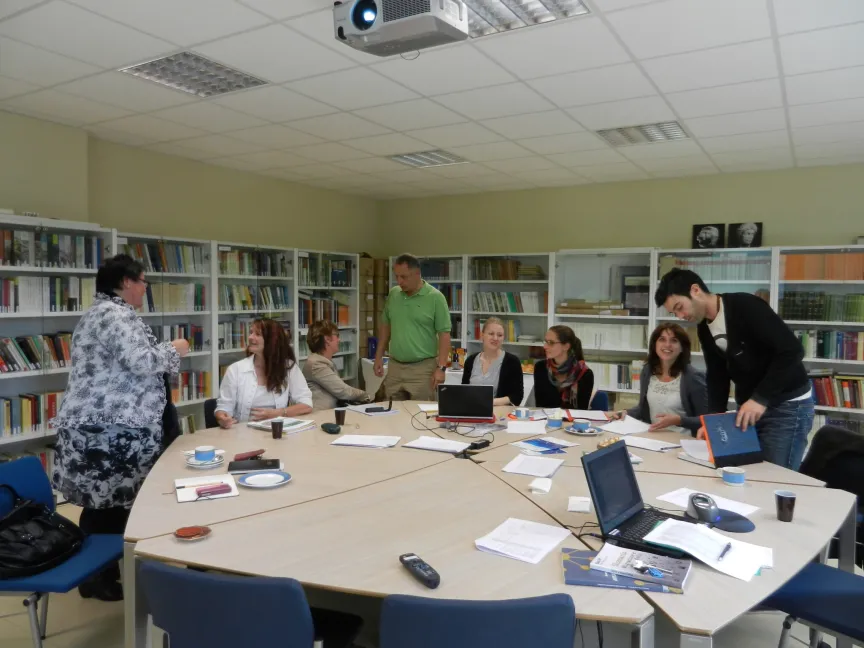 Sieben Menchen sitzen rund um einen großen Tisch in einem Büro